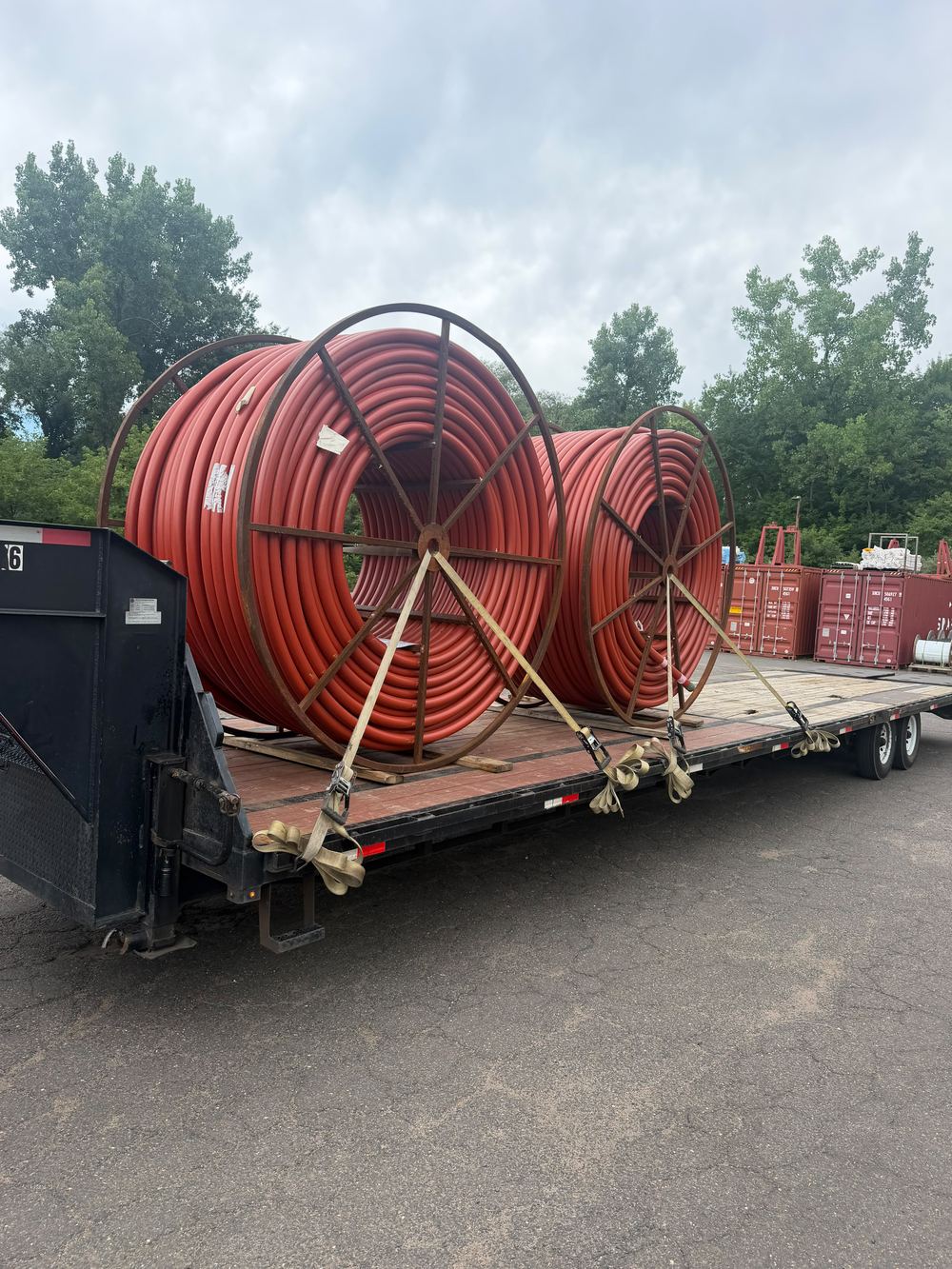 Two large spools of red conduit strapped to a gooseneck flatbed