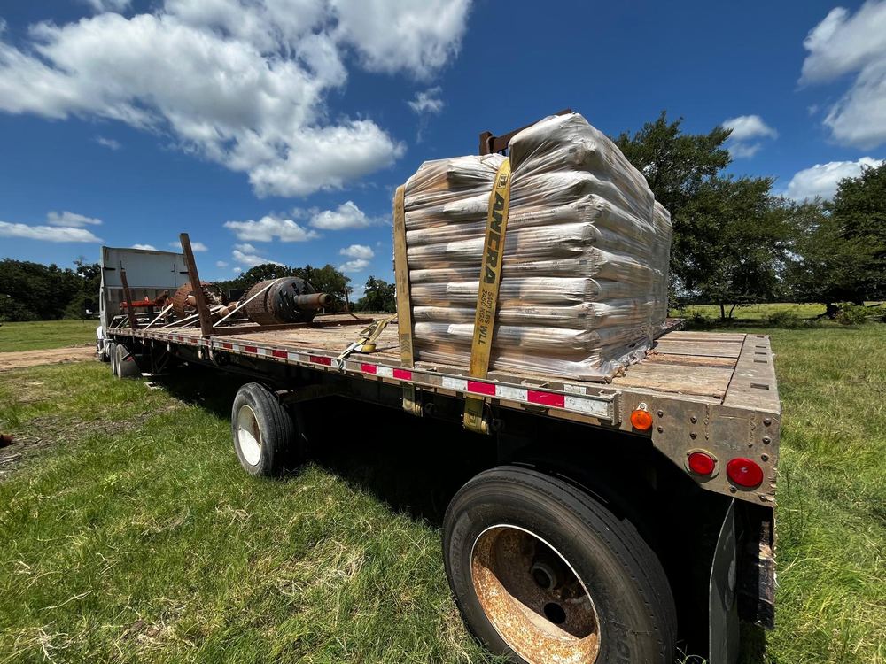 A shrink-wrapped pallet of bags strapped down on a flatbed trailer under a blue sky