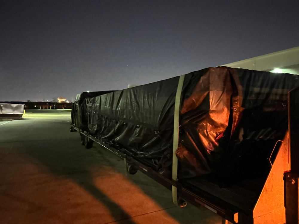 A tarped flatbed load secured under work lights at night